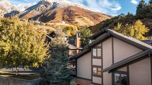 A modern building with a sloped roof, surrounded by trees and a mountain backdrop.