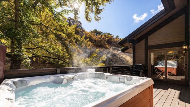 A hot tub on a wooden deck with a view of trees and a building in the background.