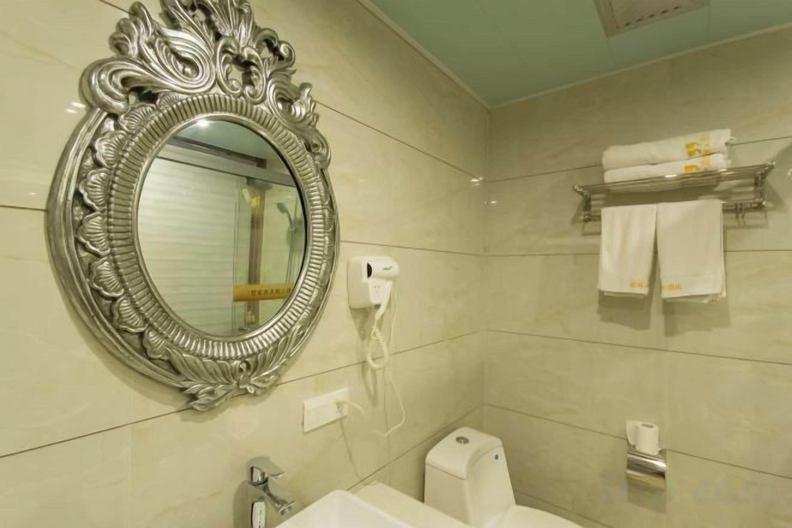 Een badkamer met een grote, versierde spiegel, een wastafel, een handdoekrek met handdoeken en een toilet.