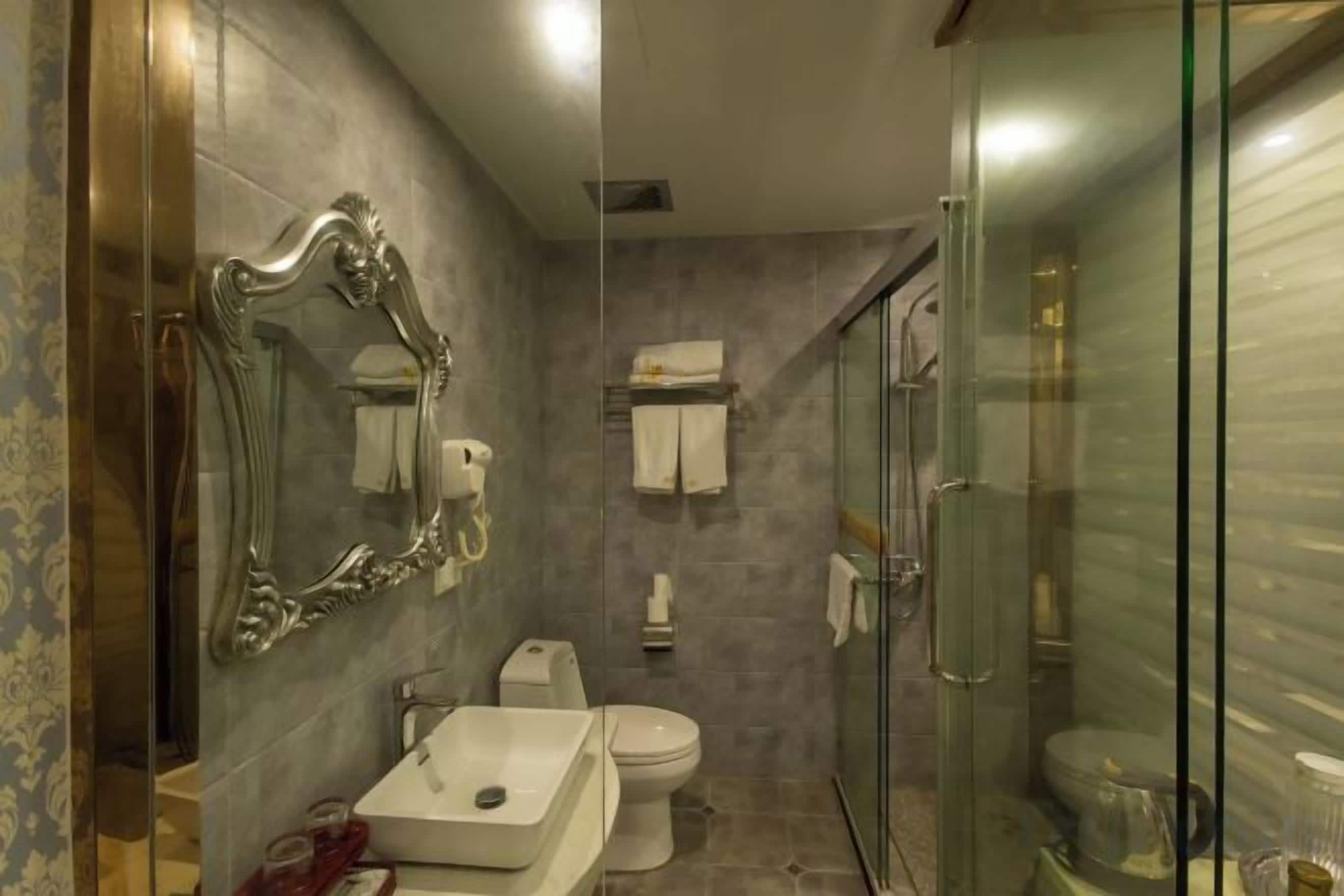 Ein Badezimmer mit Duschkabine aus Glas, Waschbecken, Toilette und Spiegel mit aufwendiger Rahmung.