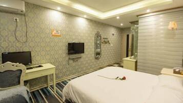 A hotel room with a bed, a desk with a TV, a mirror, and a wall-mounted WiFi sign.