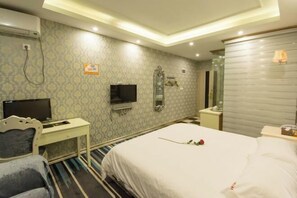 Ett hotellrum med en säng, ett skrivbord med en tv, en spegel och en väggmonterad skylt som visar att det finns Wi-Fi.