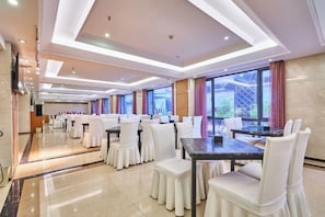 Un comedor de hotel con varias mesas redondas y sillas blancas, ventanas amplias y un diseño moderno del techo.