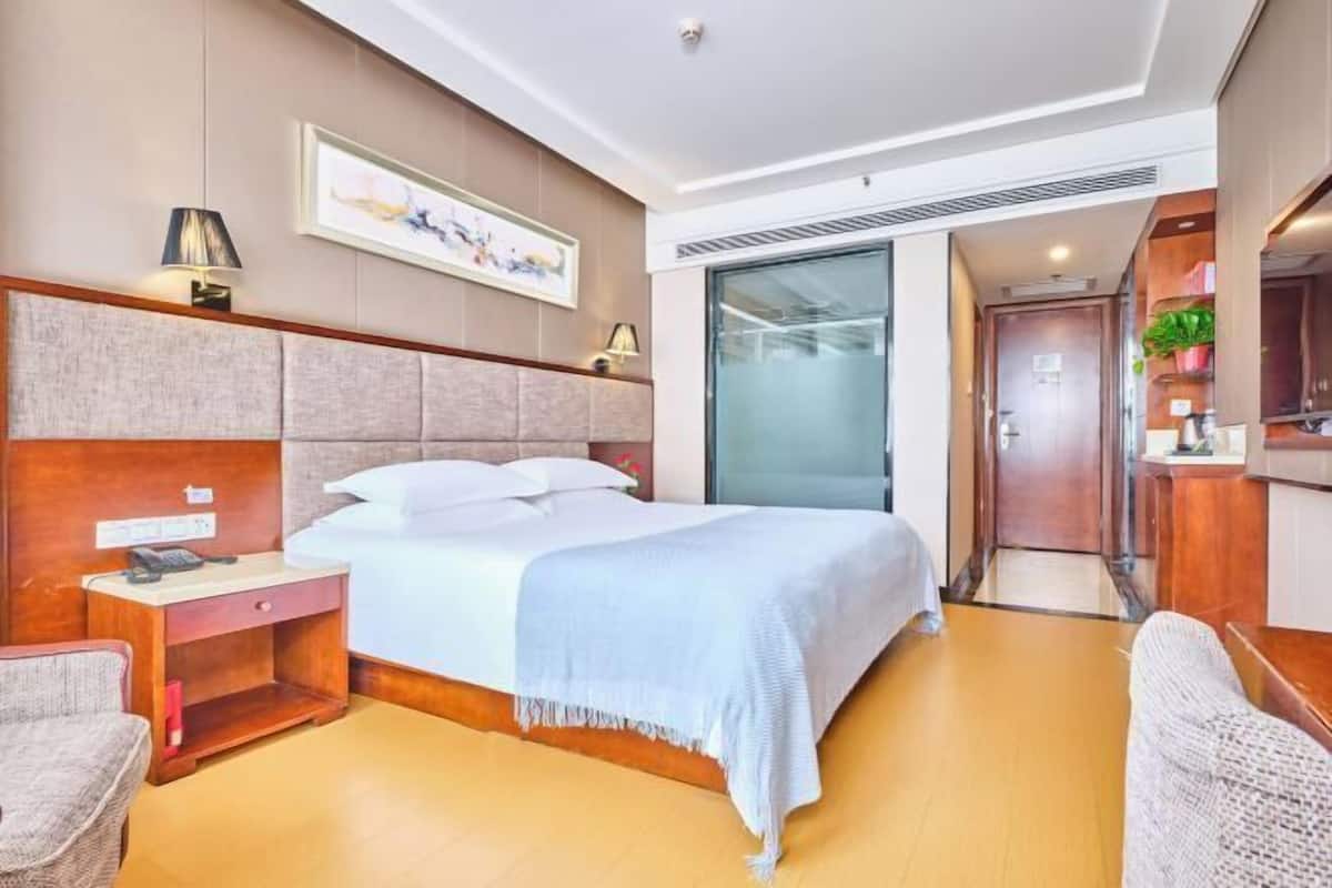 Une chambre d’hôtel moderne, dotée d’un grand lit, d’une table de chevet, d’une chaise et donnant sur le couloir.