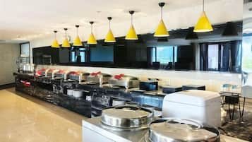 A buffet setup with multiple serving stations, overhead lighting, and a large window providing natural light.