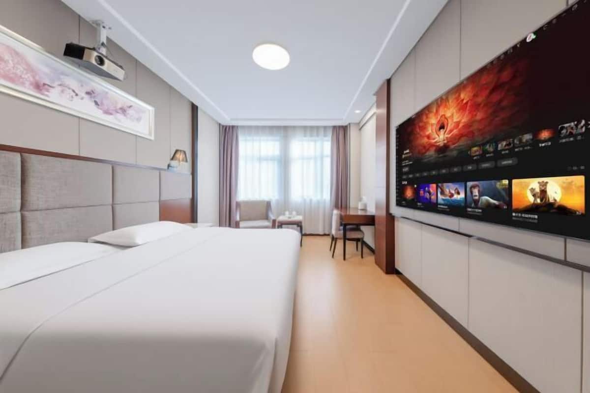 Une chambre d’hôtel avec un grand lit, un bureau avec une chaise, un téléviseur à écran plat fixé au mur et une fenêtre avec des rideaux.
