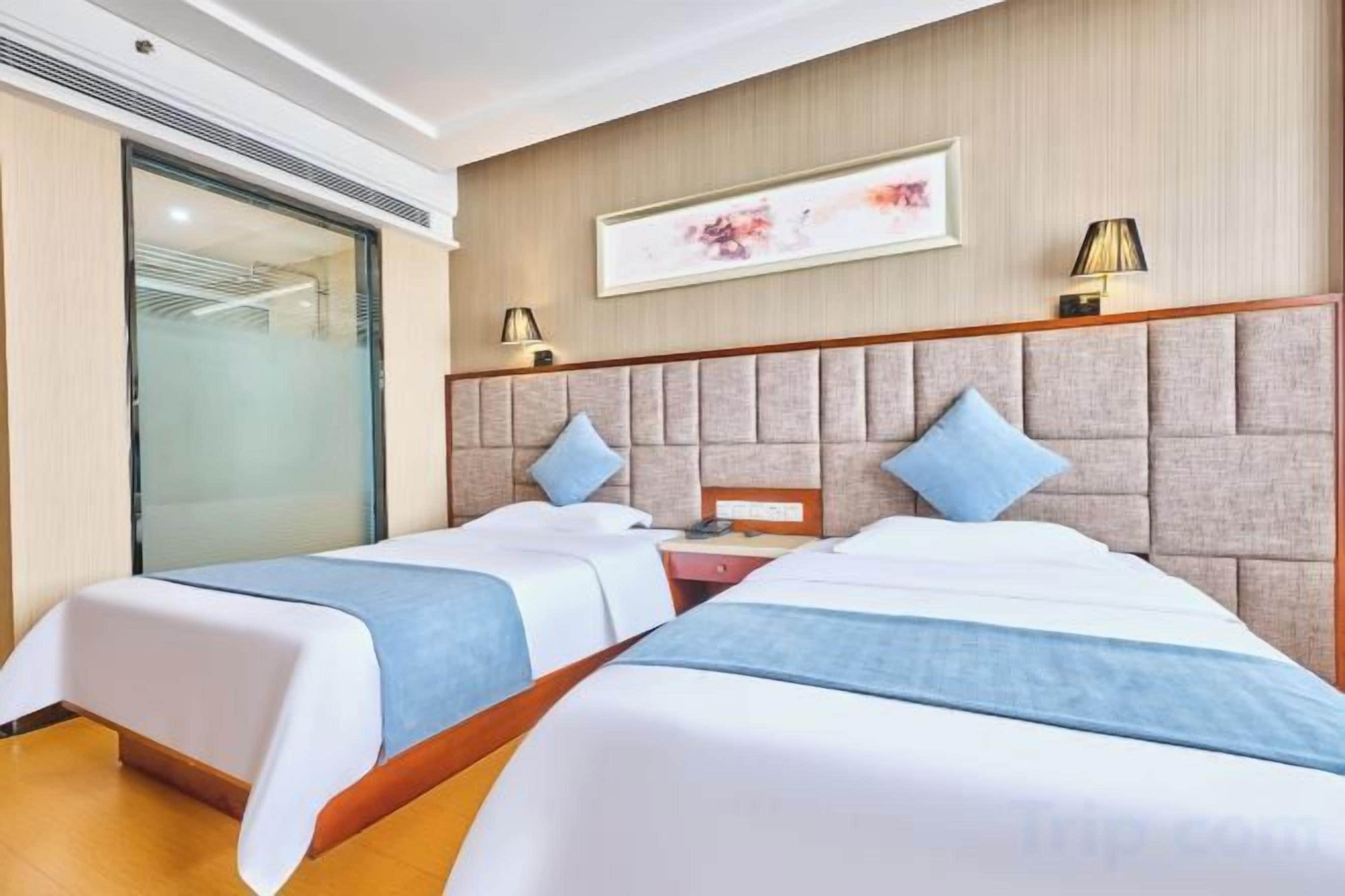 Habitación de hotel con dos camas, cabecera de madera, mesita de noche y lámpara de pared.
