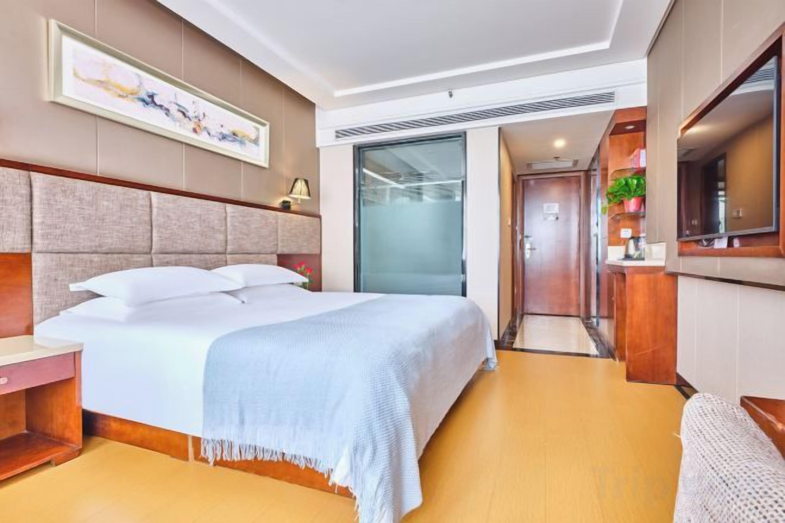 Habitación de hotel con cama, mesita de noche y vista al pasillo.