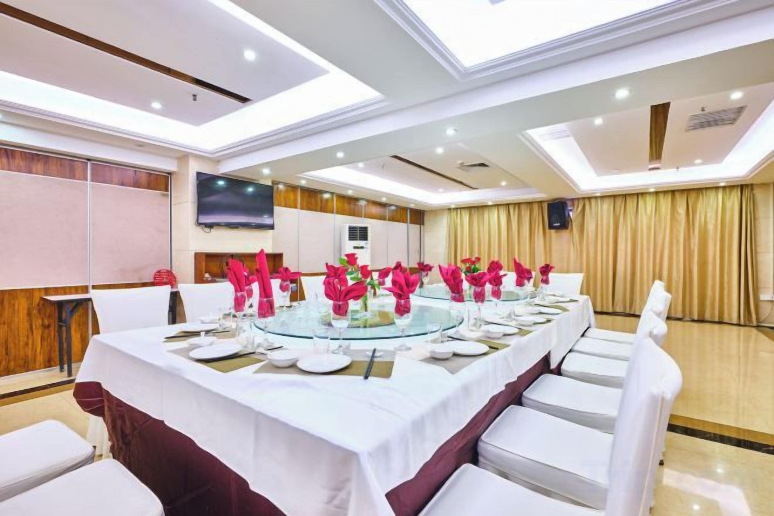 Un salón de conferencias con una larga mesa dispuesta para una reunión, equipado con sillas y una pantalla de televisión.