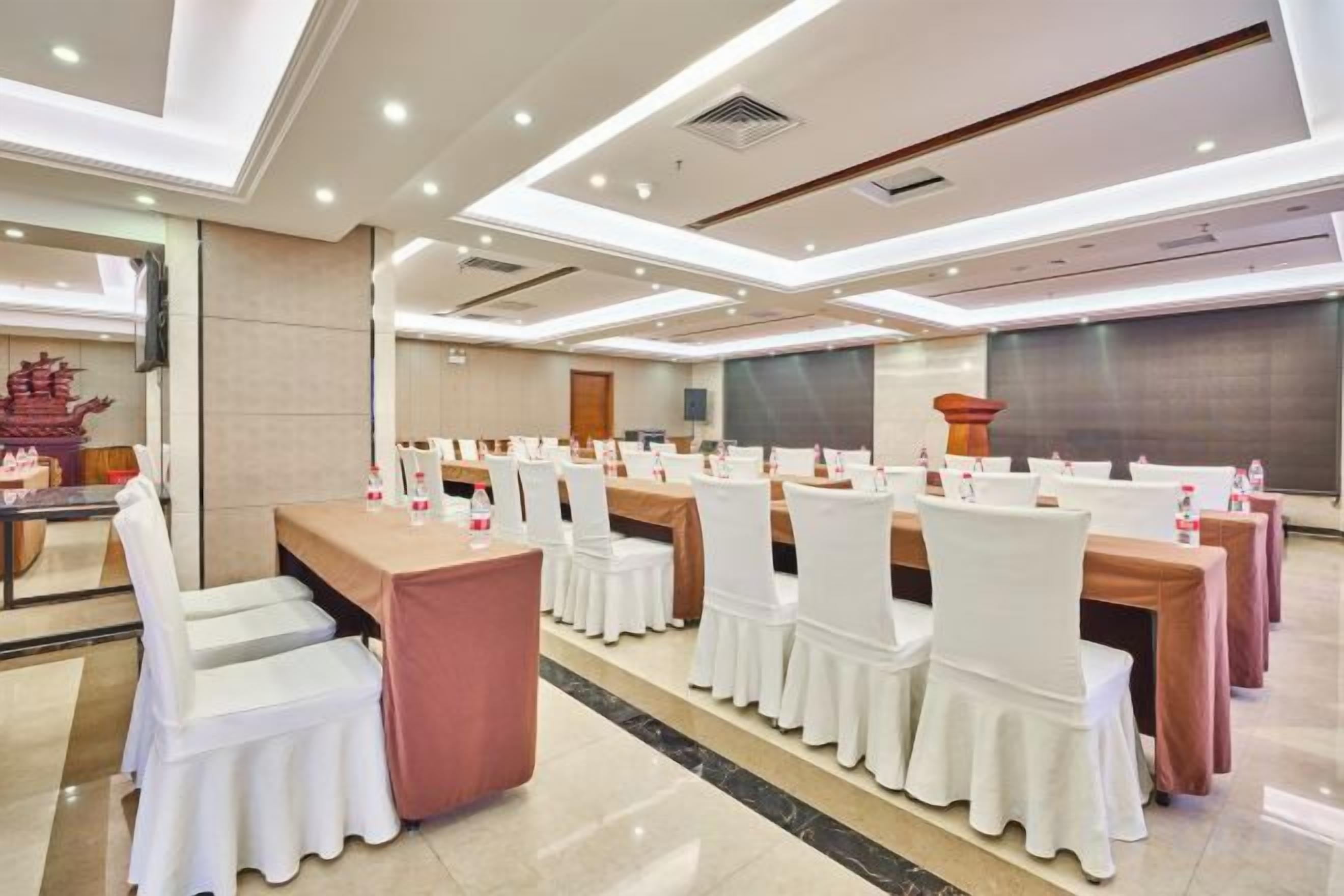 A conference room with multiple tables and chairs, a large screen, and a stage area.