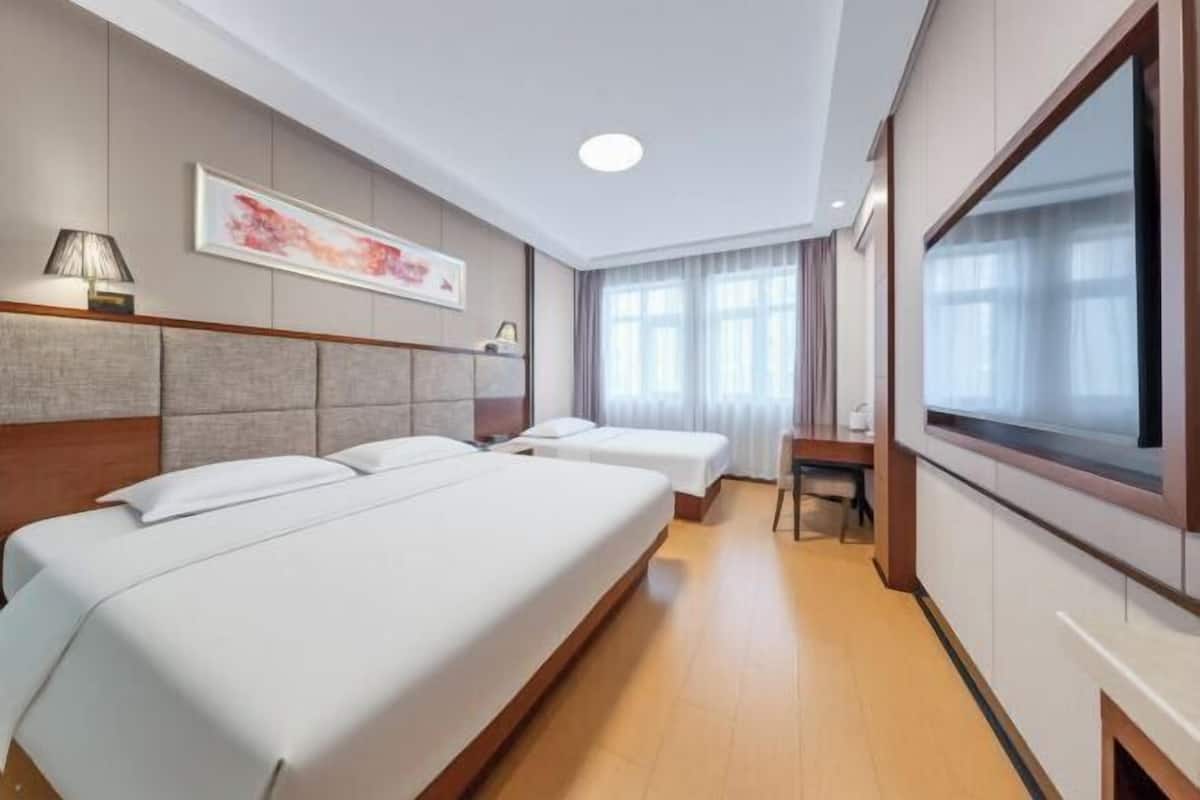 Une chambre d’hôtel avec trois lits, un bureau, une chaise, une télévision et un tableau au mur.