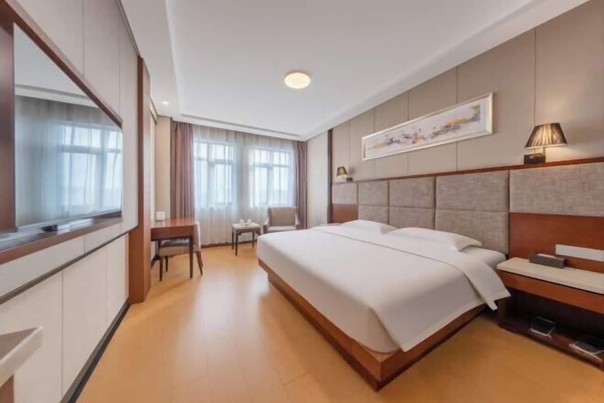 Une chambre d’hôtel avec un grand lit, un bureau, une chaise, une télévision et un tableau au mur.
