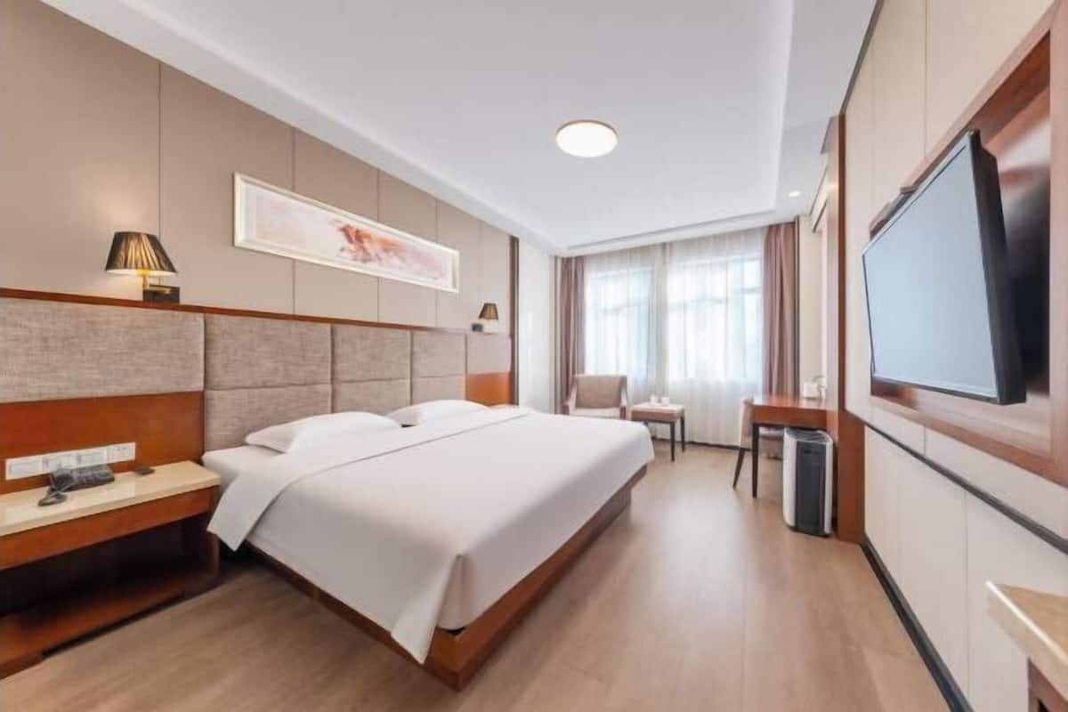 Une chambre d’hôtel avec un lit, une table de chevet, une lampe, une télévision et une fenêtre avec des rideaux.