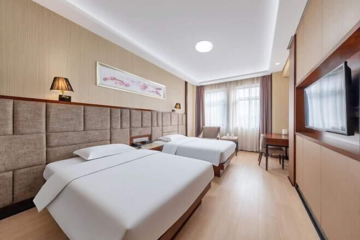 Une chambre d’hôtel avec deux lits, un téléviseur à écran plat, un bureau et une fenêtre avec des rideaux.