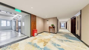 A hotel corridor with a patterned carpet, wooden panel walls, and a red trash bin. - Runxi Yueju Hotel (Zhengzhou Erqi Wanda Plaza) (Zhengzhou)
