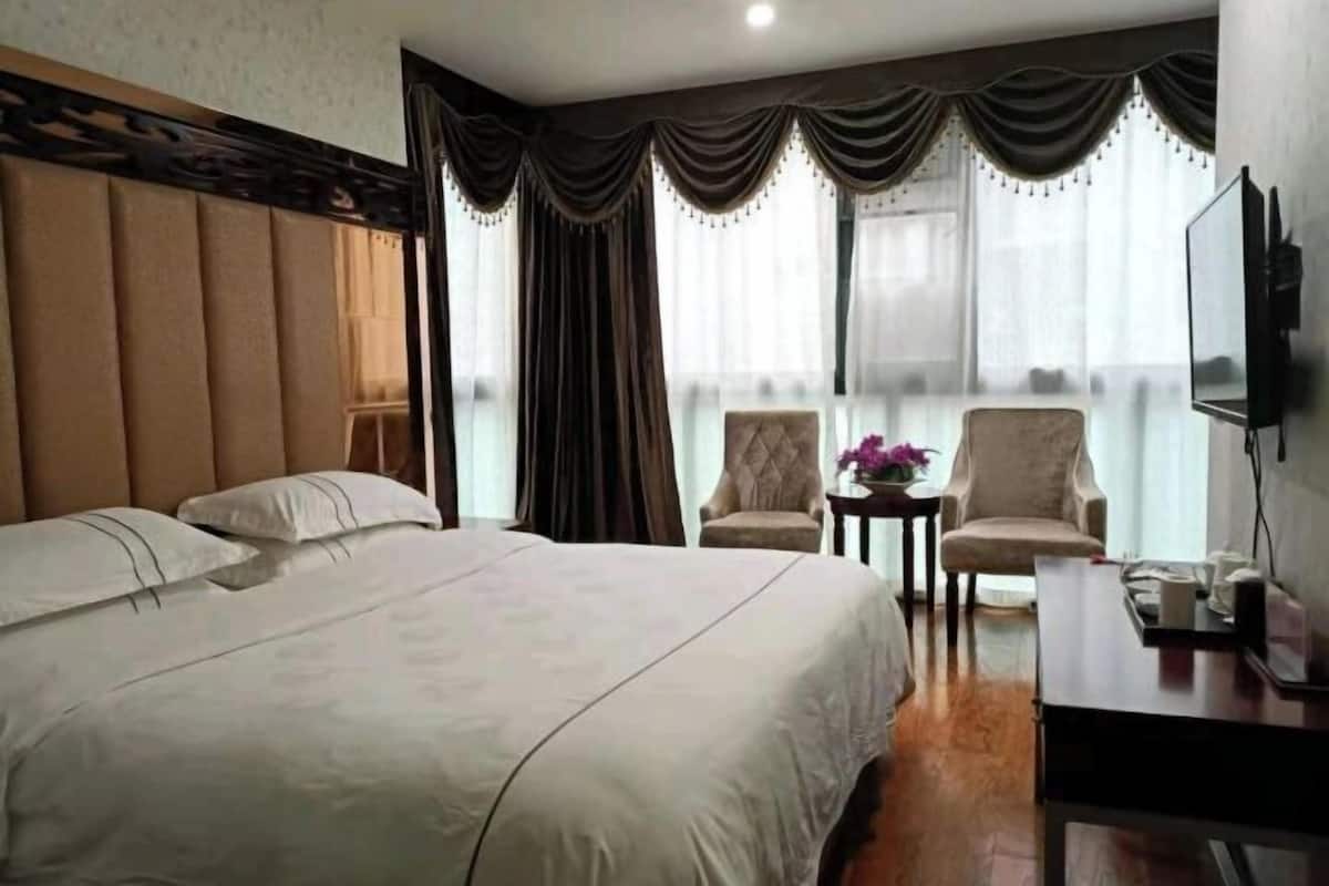A hotel room with a large bed, two armchairs, a small table, and a TV.