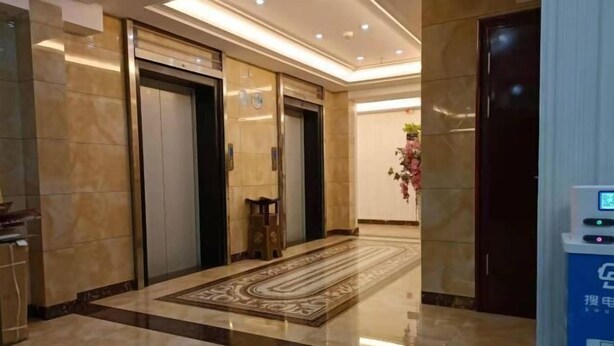 Una hall d'albergo con due ascensori, un tappeto decorato e una zona reception con display digitale.