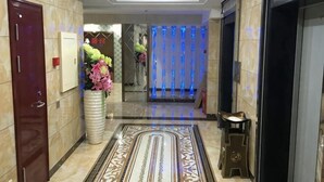 Una hall d'albergo con una reception, un vaso grande di fiori, un tappeto decorato e un ascensore.