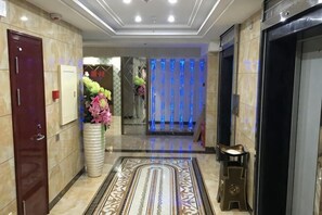 Un vestíbulo de hotel con una recepción, un jarrón grande de flores, una alfombra estampada y un ascensor.