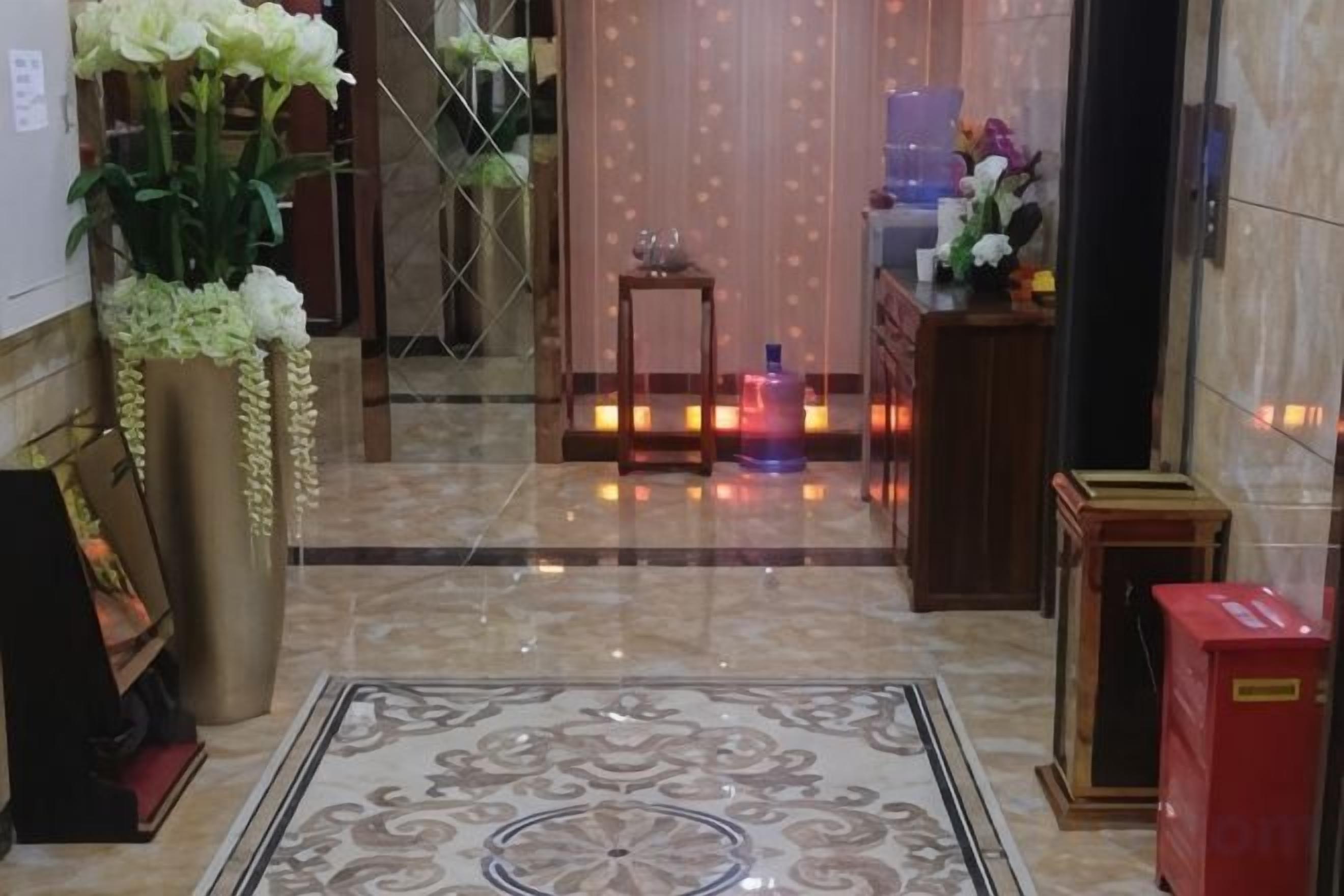 A hotel lobby with a marble floor, a reception desk, and a large potted plant.