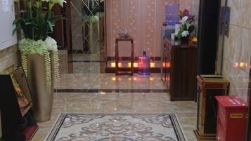 A hotel lobby with a marble floor, a reception desk, and a large potted plant.
