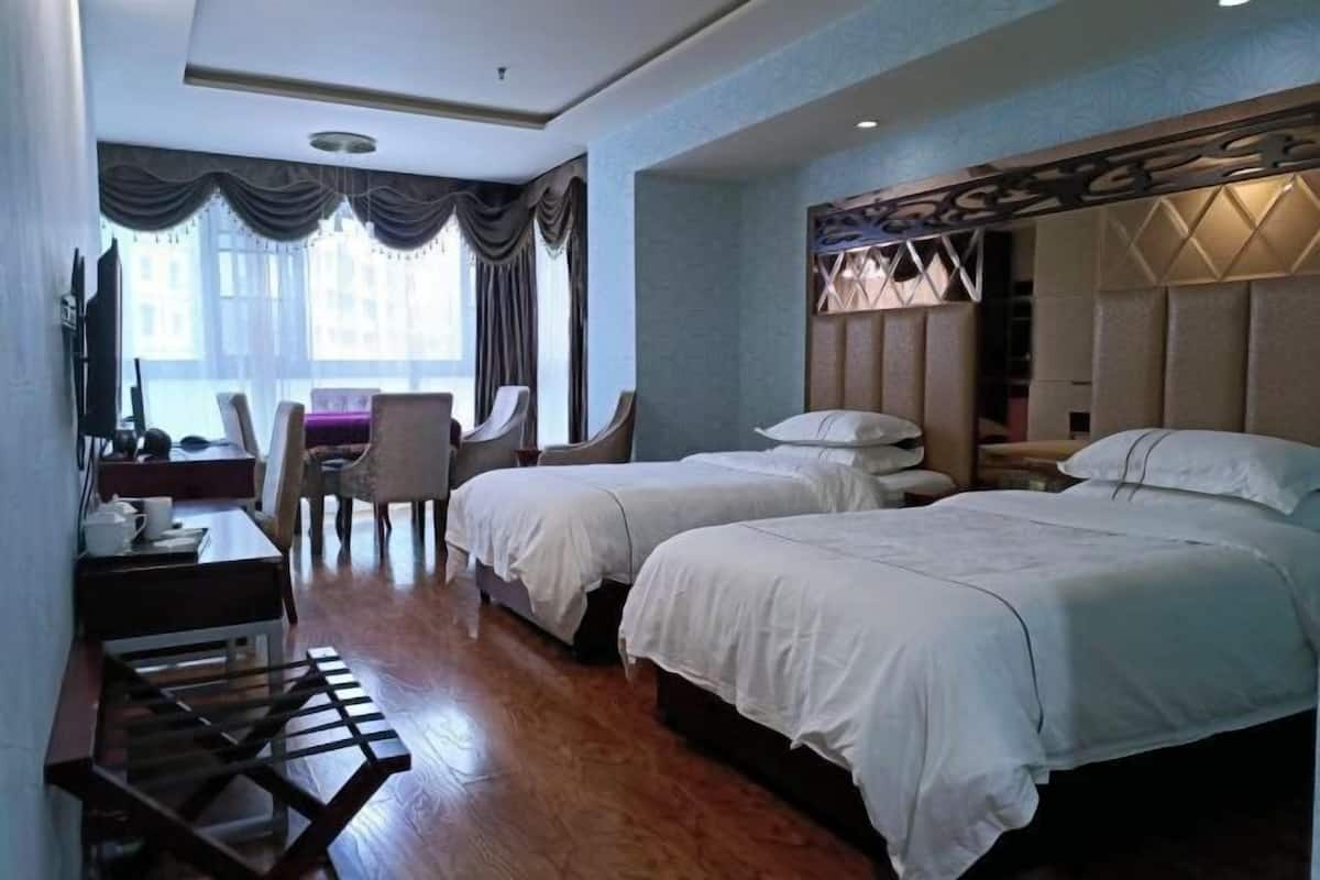 A hotel room with two beds, a desk with a chair, a TV, and a window with curtains.