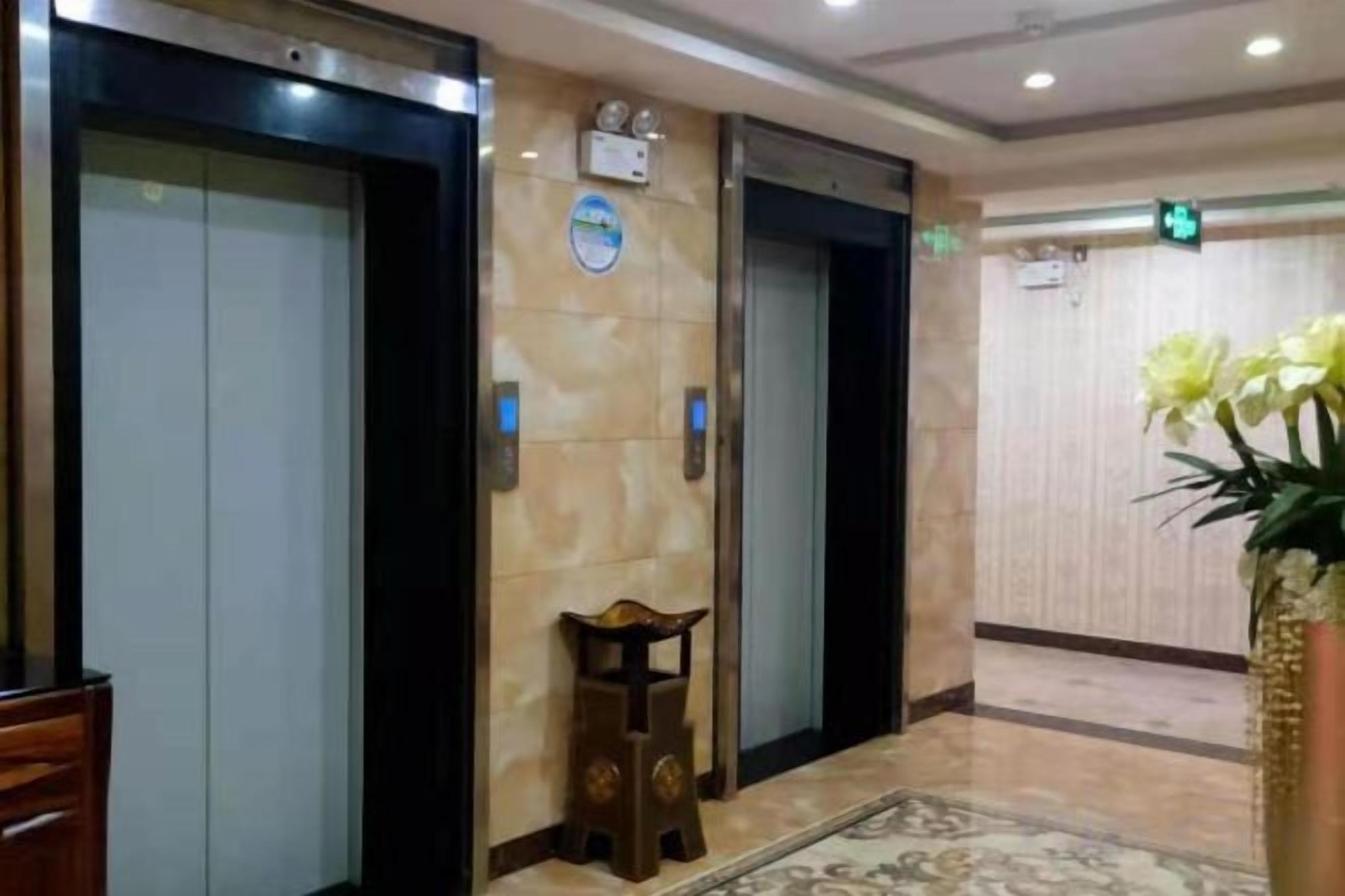 A hotel lobby with elevators, a reception desk, and a decorative plant.