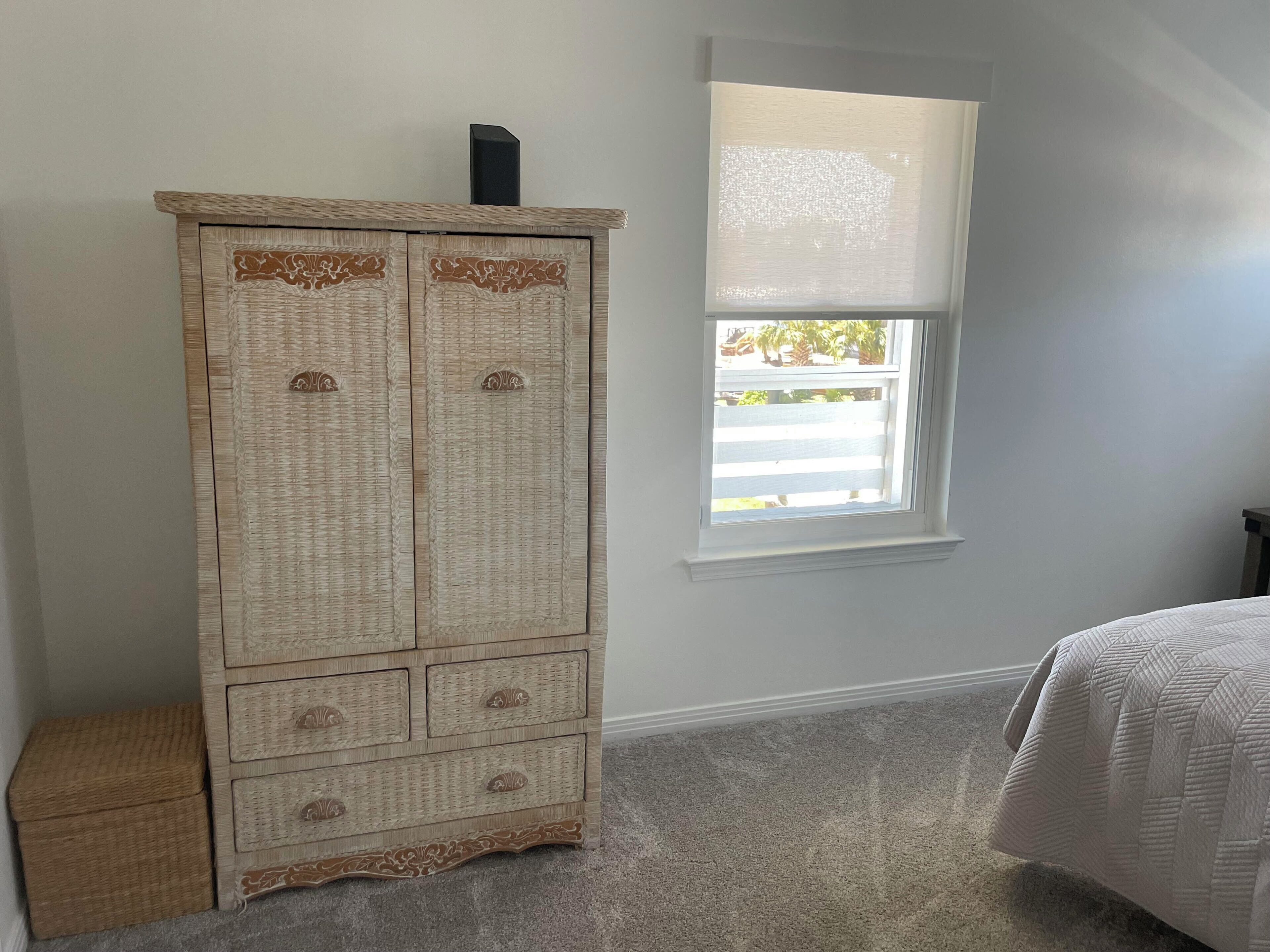 Un dormitorio con un armario grande de madera, una ventana con persianas y una cama con colcha.