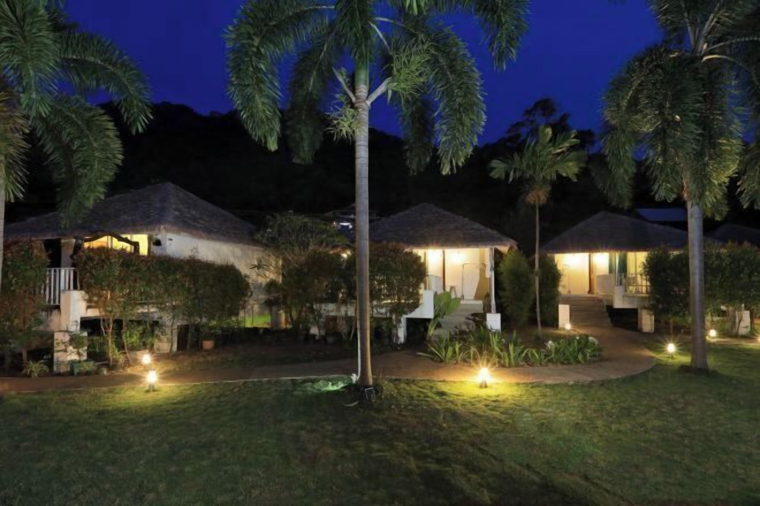 A resort with thatched-roof huts, well-lit pathways, and lush greenery.