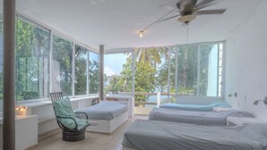 A room with two beds, a chair, and large windows.
