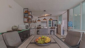 A modern kitchen with a dining area, featuring a central island with a fruit bowl, pendant lighting, and a brick accent wall.