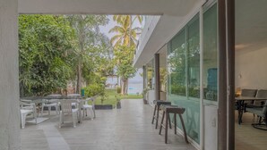 An outdoor patio with a dining area, a view of the sea, and a glass wall.