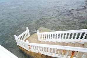 A staircase leading to a body of water with clear water, white balustrades, and stone steps. - RedDoorz Plus @ Billys Resort Oslob (Oslob)