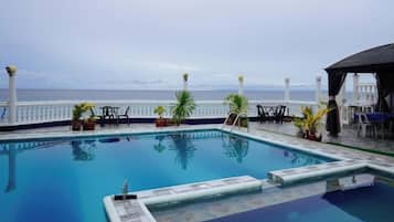 A swimming pool with a view of the sea, surrounded by potted plants and outdoor furniture.