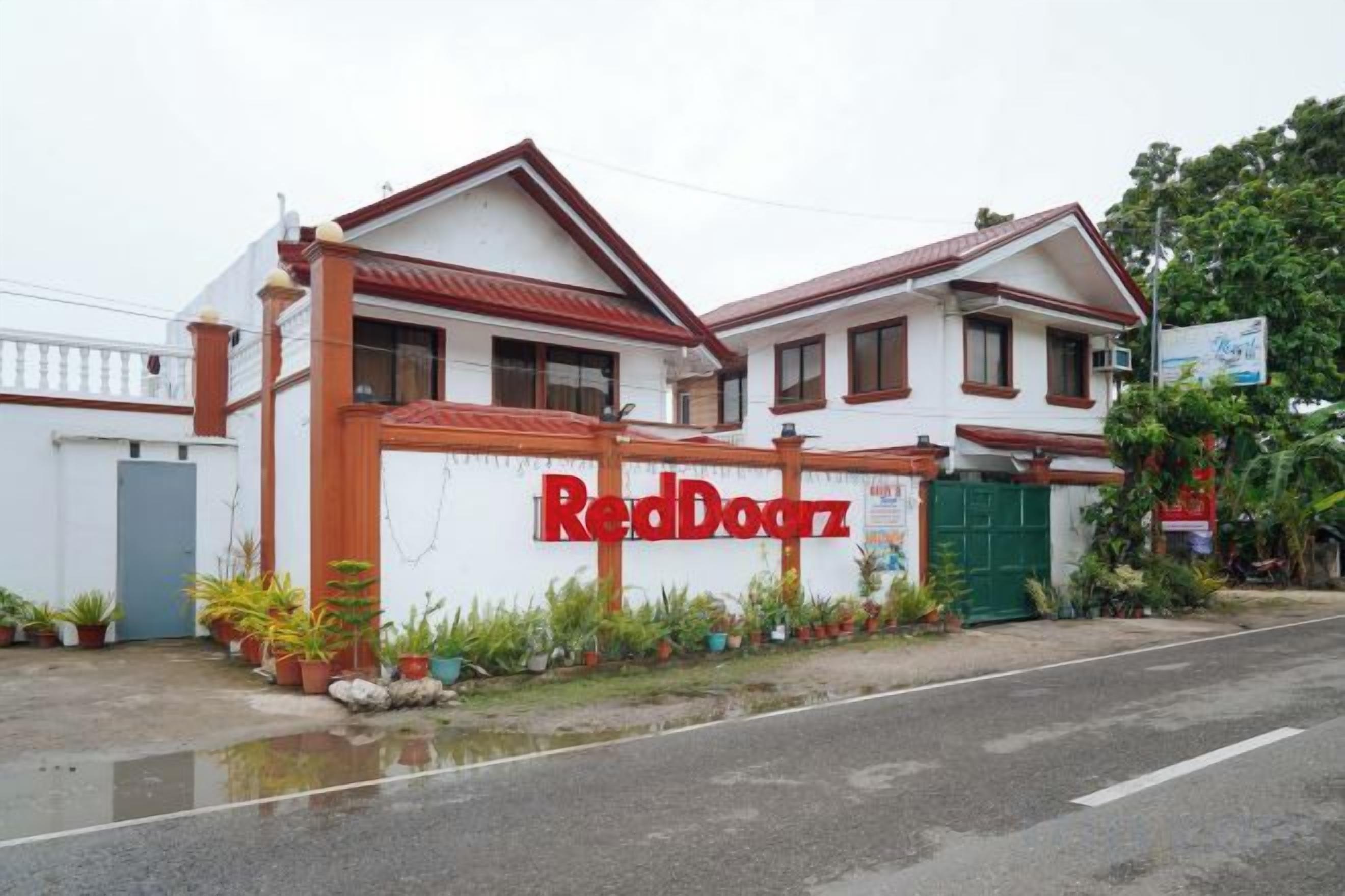 A two-story building with a red and white facade, a gated entrance, and a sign that reads 'RedDoorz'.