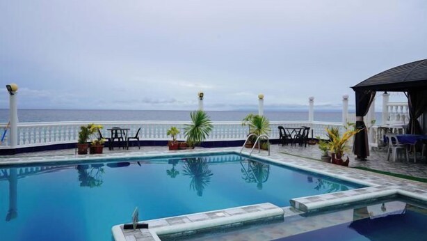 A pool with a view of the sea, surrounded by potted plants and outdoor furniture. - RedDoorz Plus @ Billys Resort Oslob (Oslob)