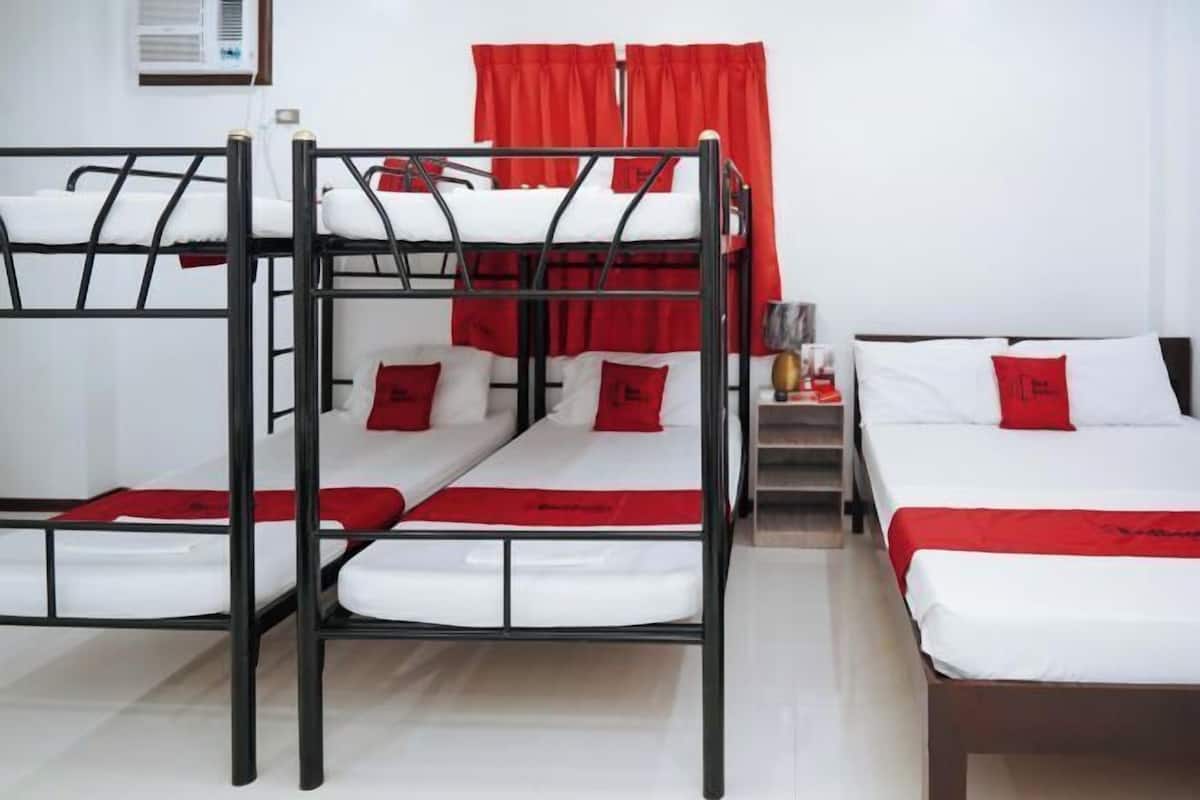 Una habitación con literas, una cama individual y una mesita de noche con lámpara.