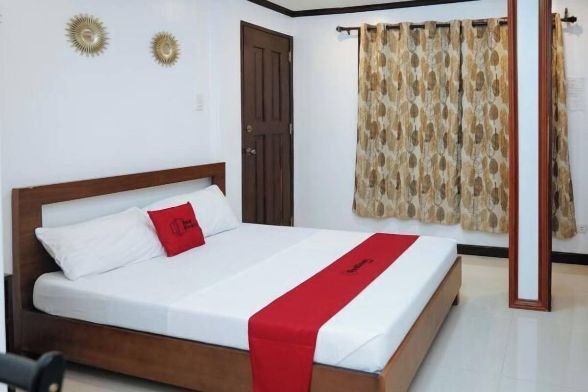 Una cama bien hecha con un cojín rojo decorativo, un cabecero de madera y una colcha blanca.