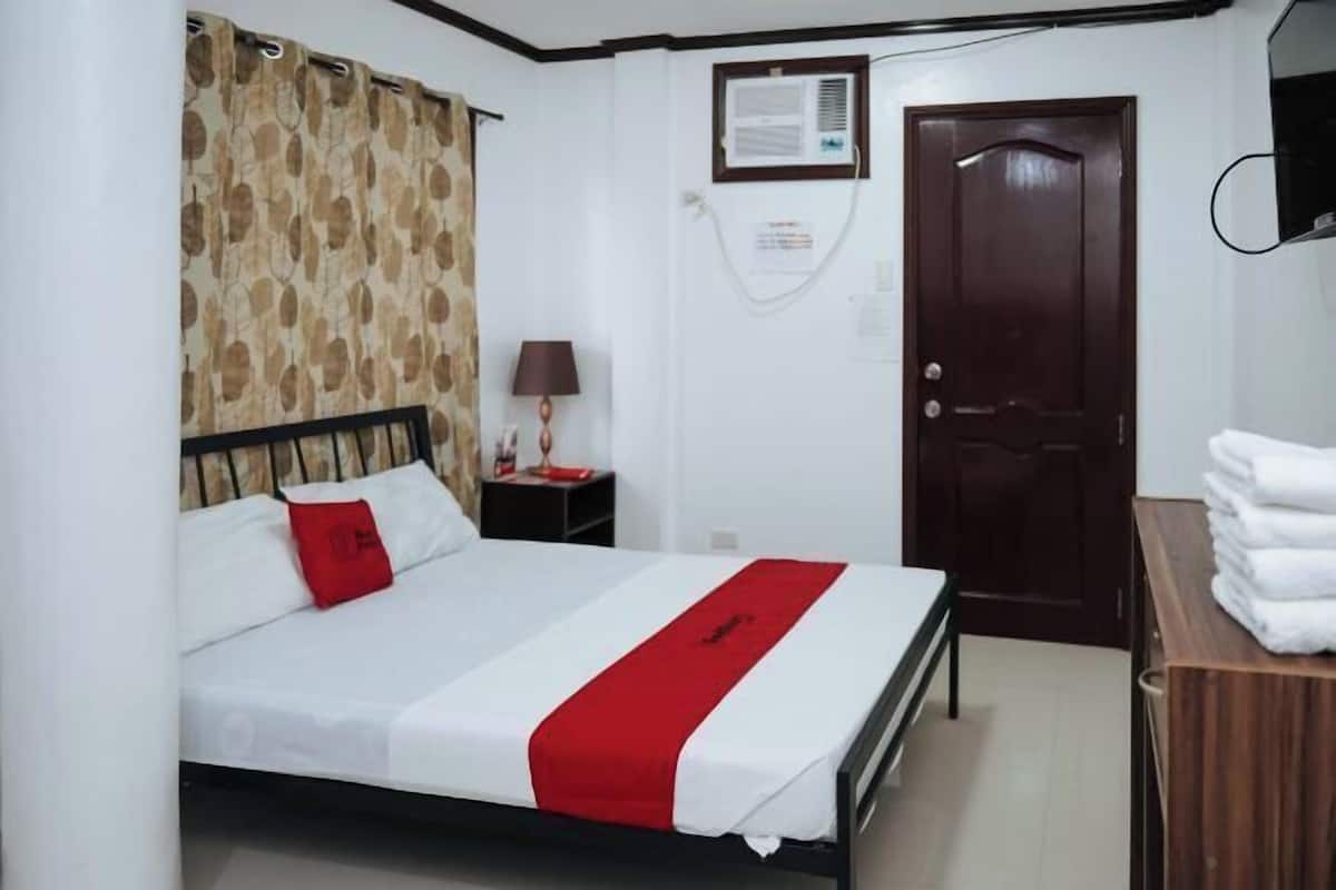 Habitación de hotel con cama, mesita de noche, lámpara, puerta y aire acondicionado instalado en la pared.