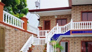 A two-story building with a staircase, white railings, and potted plants. - RedDoorz Plus @ Billys Resort Oslob (Oslob)