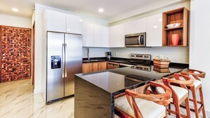 A modern kitchen with a central island, stainless steel appliances, wooden bar stools, and a decorative wall panel. - Quinta San Miguel Canal Pool Steps Beach (Nuevo Nayarit)