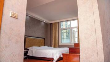 A hotel room with a bed, a nightstand, a wooden dresser, and a window with a view of buildings.