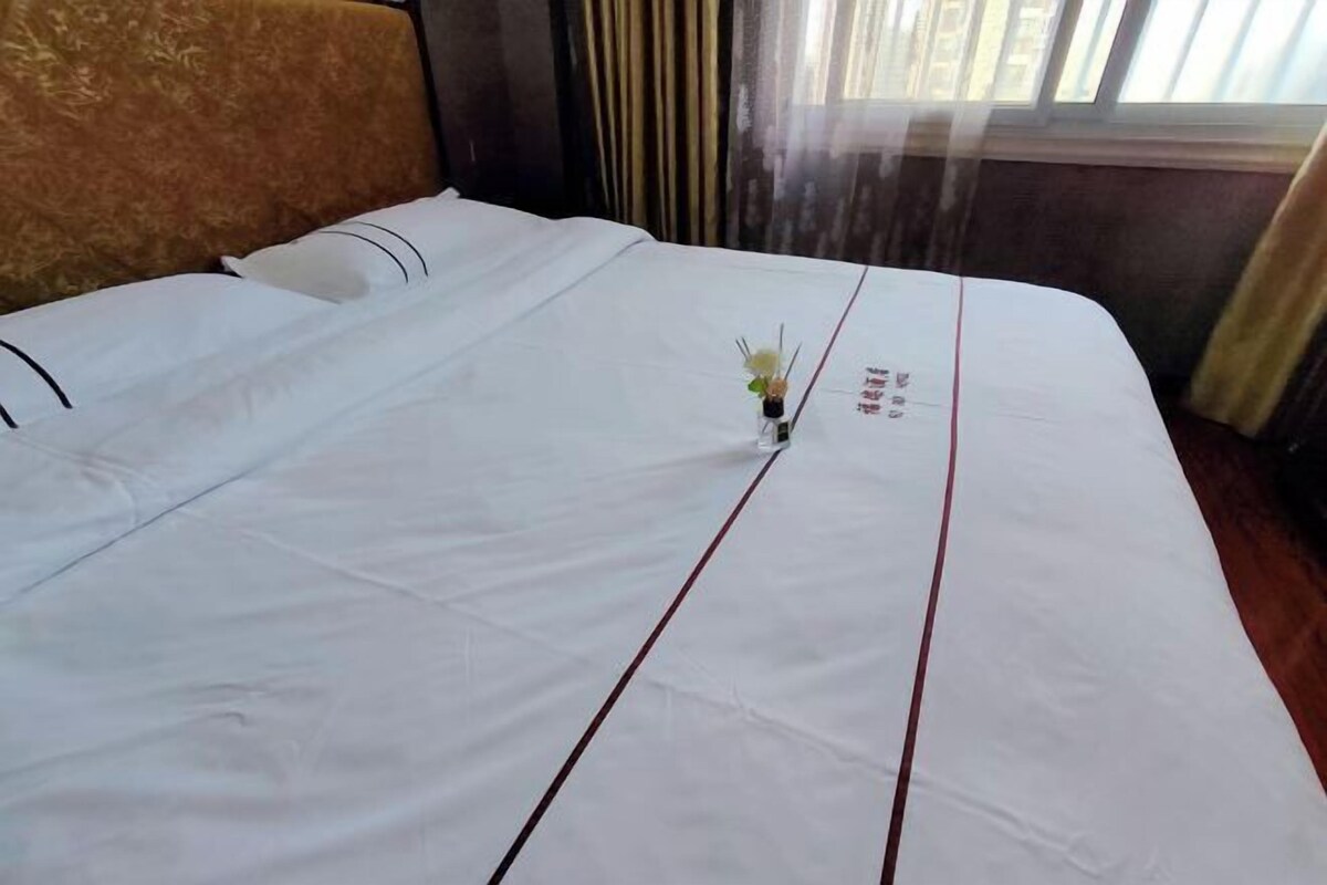 A neatly made bed with white bedding and a small vase of flowers in the center.