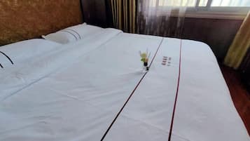 A neatly made bed with white bedding and a small vase of flowers in the center.