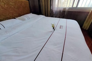 A neatly made bed with white bedding and a small vase of flowers in the center.