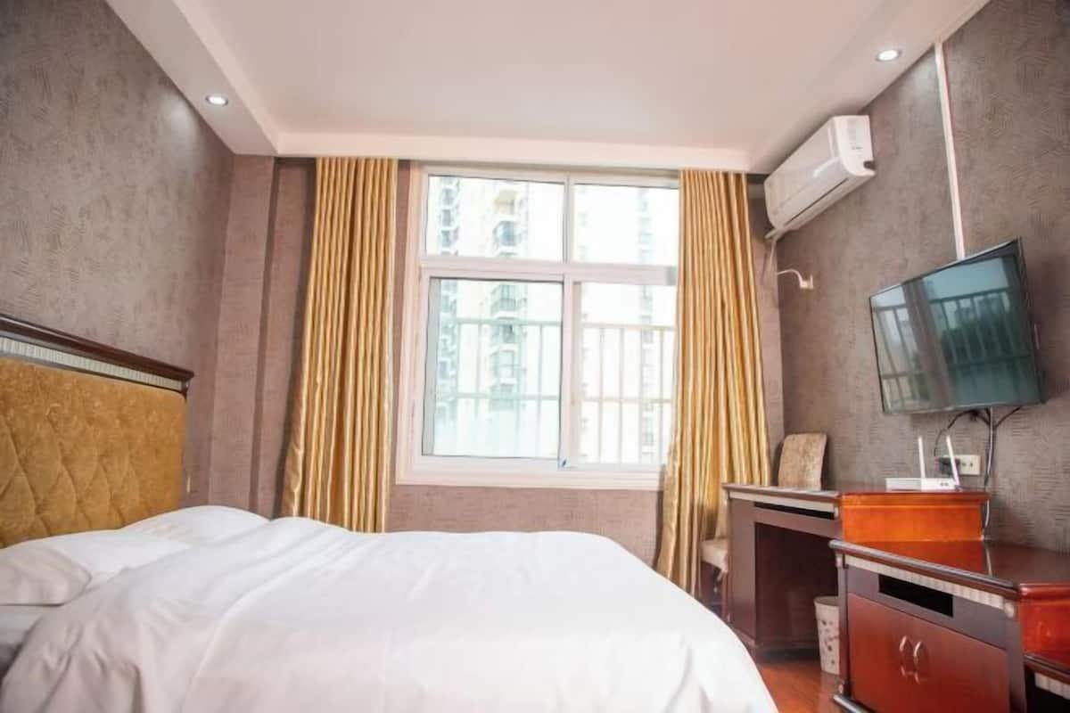 A hotel room with a bed, a desk, a TV, and an air conditioning unit.