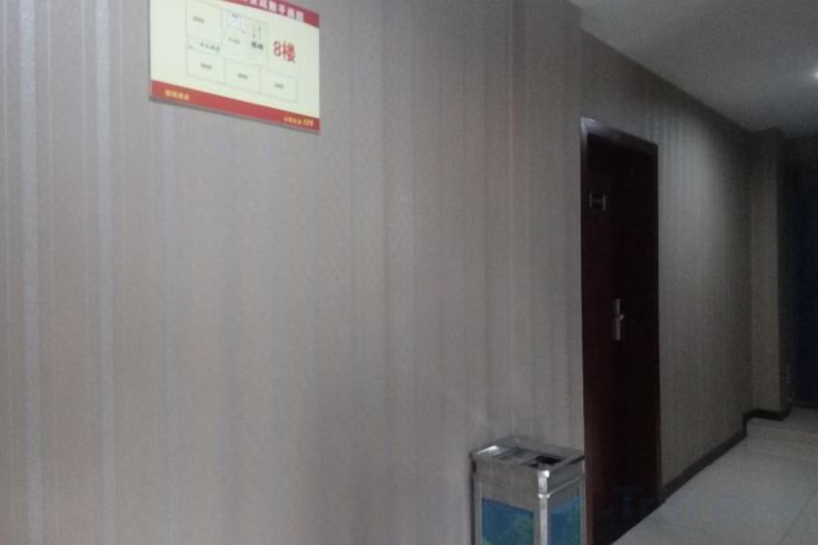 A corridor with a door on the right and a trash bin on the left.