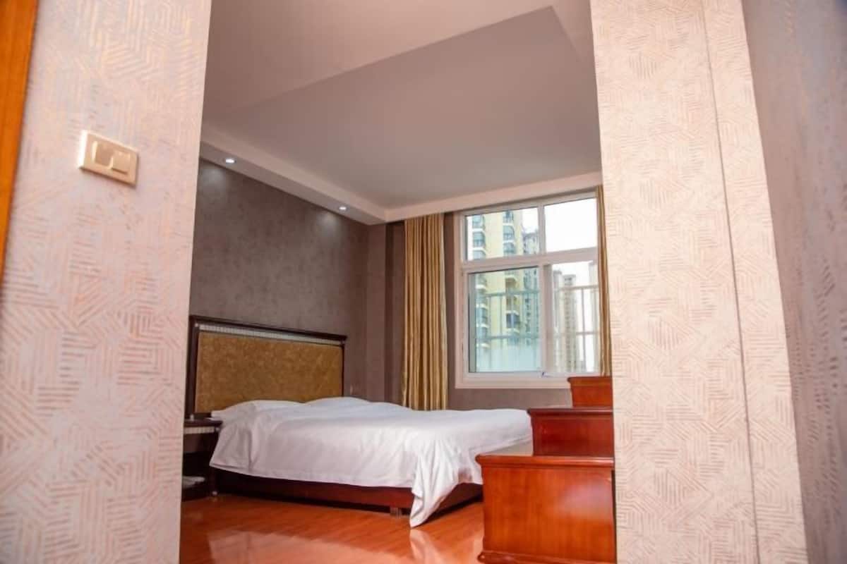 A hotel room with a bed, a nightstand, a wooden dresser, and a window with curtains.