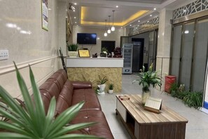 A reception area with a leather sofa, a wooden table, and potted plants. - Furui Hotel (Lichuan)