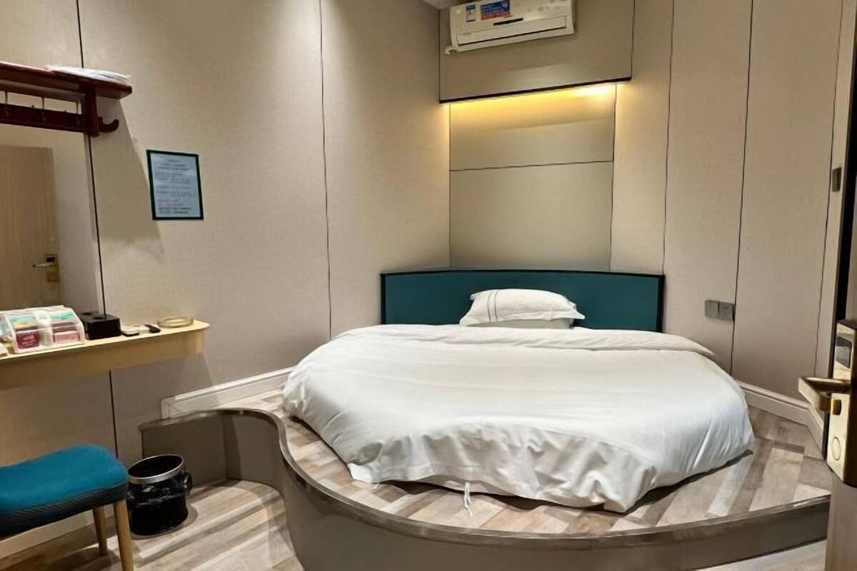 A compact hotel room with a curved bed, a small desk, and a bench.